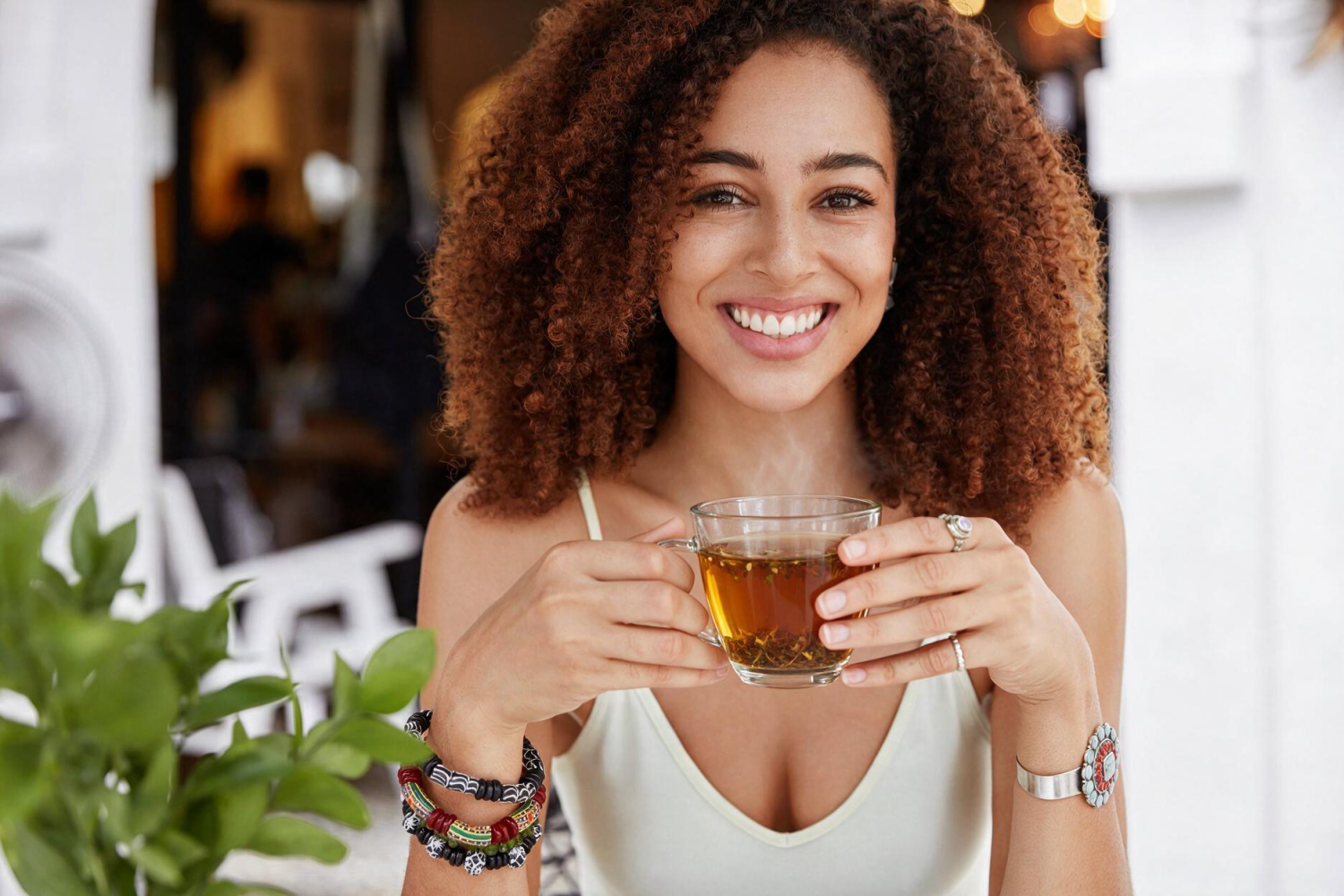 A smiling woman holding a glass cup of herbal tea
